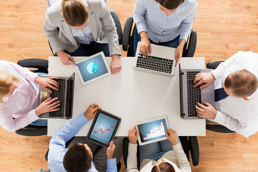 business, people and technology concept - close up of creative team with laptop and tablet pc computers displaying charts on screens sitting at table in office